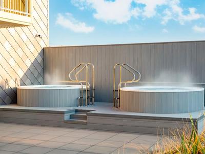 Zwei dampfende Whirlpools auf einer Terrasse bei Sonnenschein und blauem Himmel.