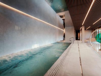 Moderner Innenpool mit blauem Wasser, grauen Wänden und Holzbalkendecke in einem Hotel.