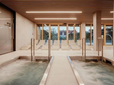 Moderner Spa-Bereich mit zwei Whirlpoolbecken, Holzdecke und großen Fenstern mit Blick auf Bäume.