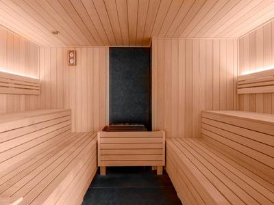 Hell beleuchtete Sauna mit Holzbänken und zentralem Holzeimer auf dunklem Boden.
