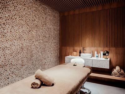 Modernes Massageraum mit Holzakzenten, Steinwand und gemütlicher Beleuchtung im Hotel.