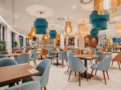 Modernes Hotelrestaurant mit stilvollen Stühlen und hängenden Lampen in warmen Farben.