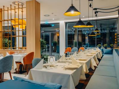 Elegantes Restaurant mit gedeckten Tischen und moderner Beleuchtung neben großen Fenstern.