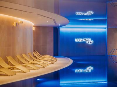 Area wellness moderna con lettini e piscina illuminata di blu.