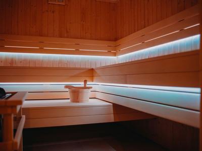 Sauna in legno con illuminazione blu indiretta e secchio di legno sulla panca