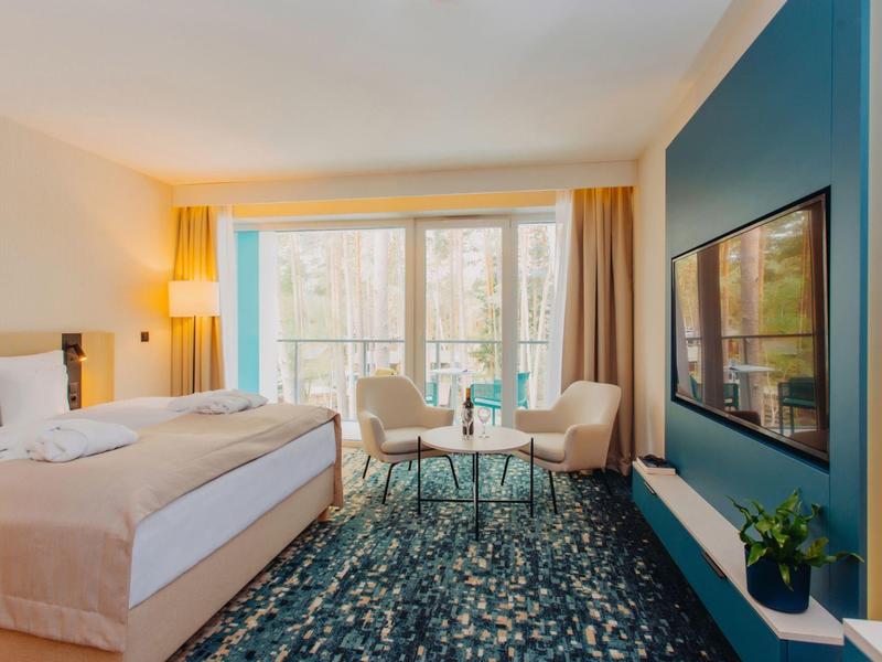 Camera d'hotel moderna con letto matrimoniale, area salotto e grande finestra con vista esterna.