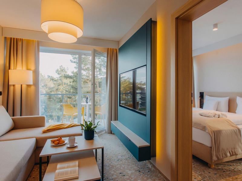 Camera d'hotel moderna con zona soggiorno e camera da letto adiacente alla luce del giorno.