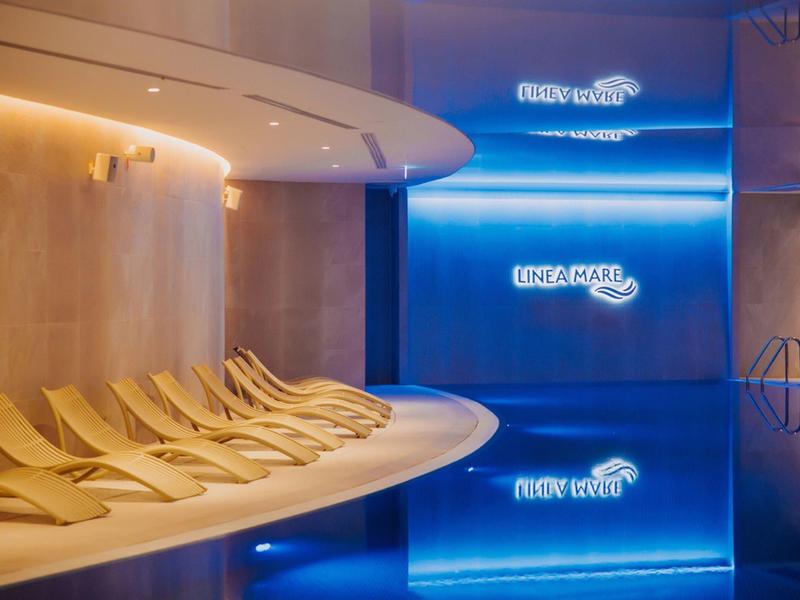 Area wellness moderna con lettini e piscina illuminata di blu.