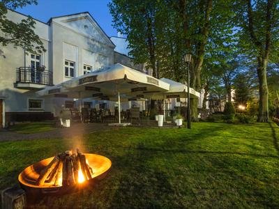 Abendaufnahme eines Hotels mit Terrasse, Feuerstelle und beleuchtetem Garten.
