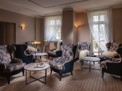 Elegantes Hotelzimmer mit bequemen Sesseln, Couchtischen und weichen Vorhängen an Fenstern.