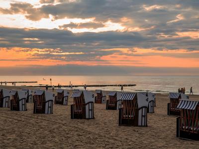 Pláž s mnoha plážovými křesly při západu slunce a zataženou oblohou nad mořem.