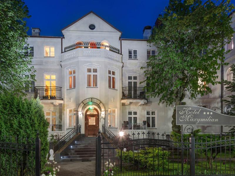 Osvětlená bílá budova hotelu se zahradou a schody za soumraku.