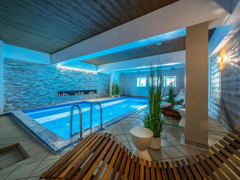 Moderní vnitřní bazén s lehátky, rostlinami a nepřímým osvětlením v hotelu.