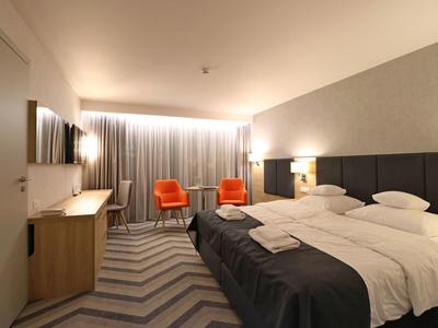 Camera d'hotel moderna con letto matrimoniale, due poltrone arancioni e una scrivania.