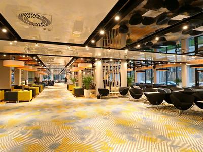 Moderner Hotel-Lobbybereich mit gelben Sesseln und schwarzen Hängesesseln auf gemusterter Teppichfläche.