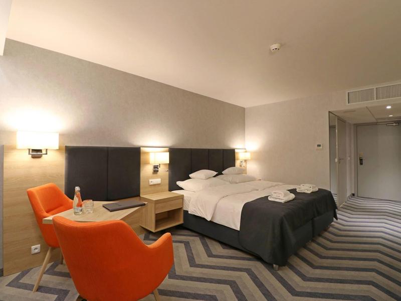 Camera d'albergo moderna con letto matrimoniale, due poltrone arancioni e tappeto a motivo zigzag.