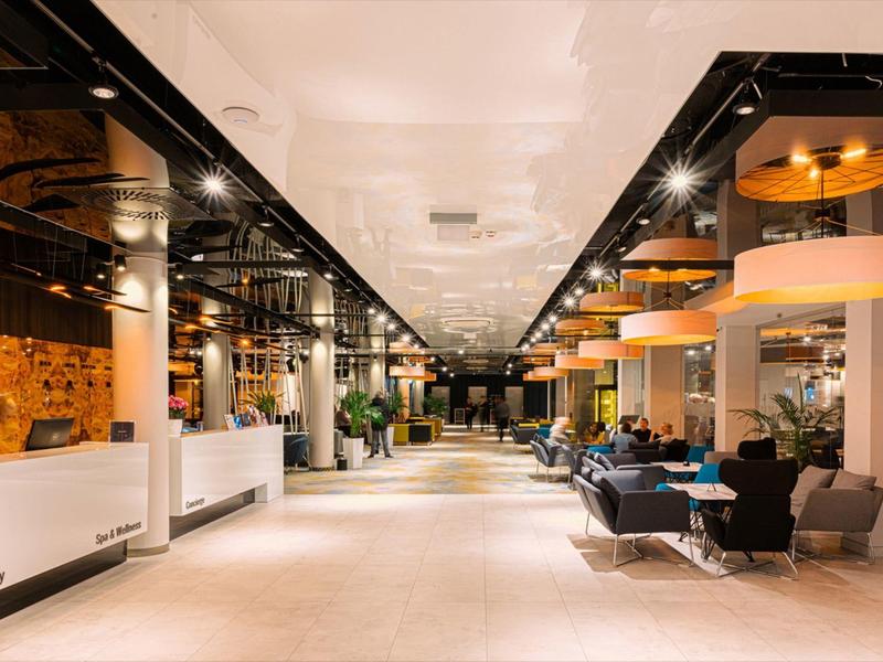 Area lobby dell'hotel moderna e spaziosa con aree salotto e illuminazione luminosa.