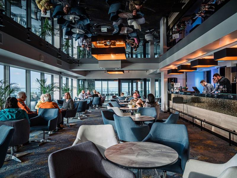 Bar dell'hotel moderno con ospiti, poltrone lounge e grandi finestre con vista.