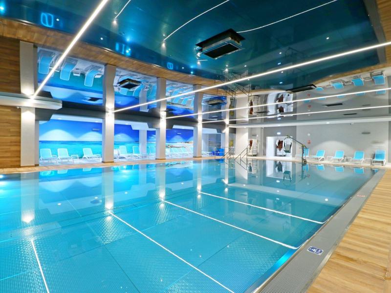 Piscina interna moderna con acqua blu e pavimento in legno chiaro in un hotel