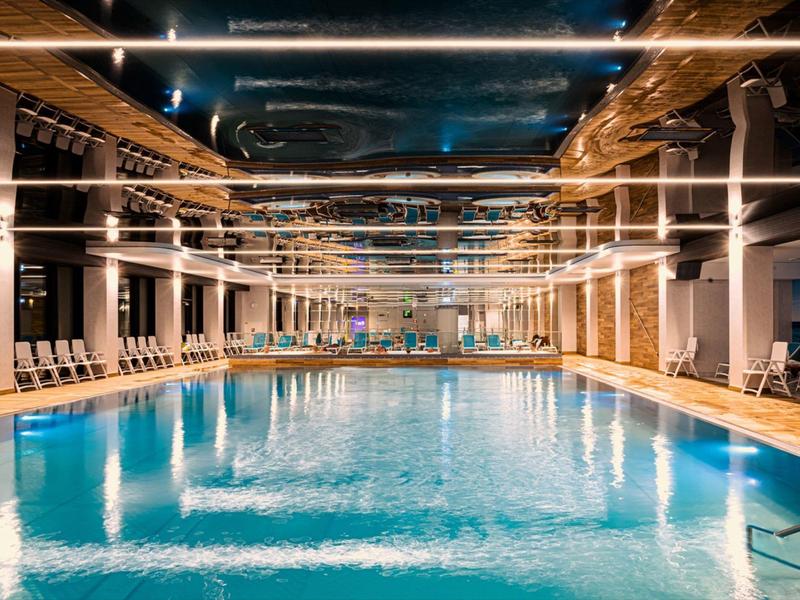 Piscina coperta luminosa con lettini e illuminazione moderna al soffitto