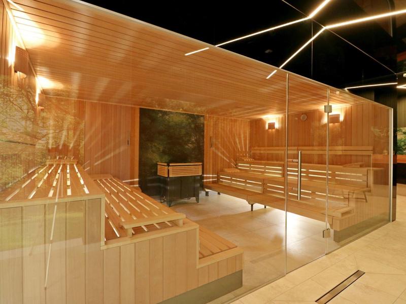 Vista interna di una sauna moderna con panche in legno e illuminazione calda.