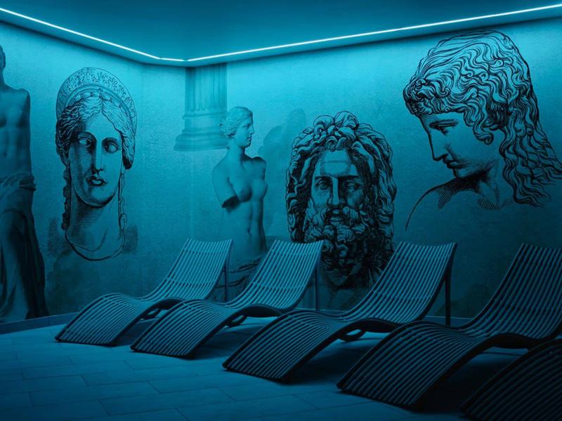 Area relax con lettini e arte murale di statue romane sotto luce blu