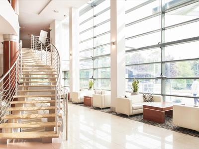 Vestíbulo de hotel luminoso con grandes ventanas, escalera y asientos blancos.