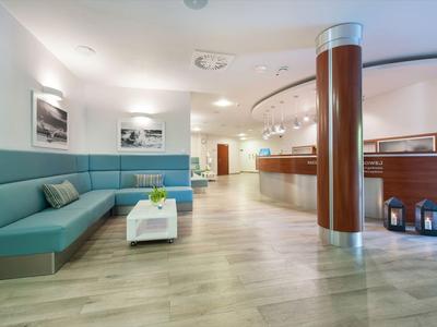 Moderna recepción de hotel con área de asientos, mostrador y suelo de madera clara.