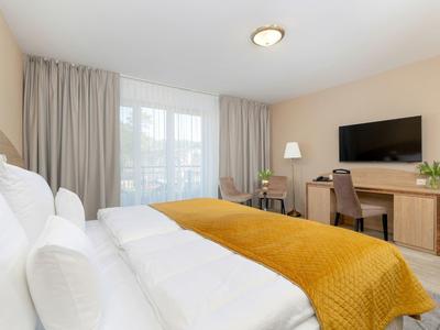 Modernes Hotelzimmer mit großem Bett, gelber Decke, Schreibtisch, Stuhl und Fernseher an der Wand.