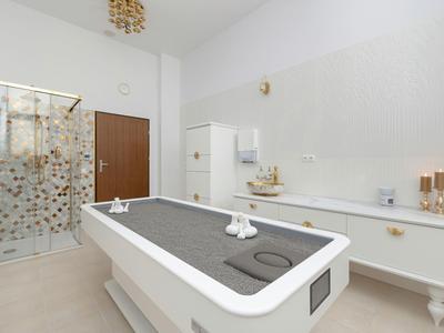 Helles Wellnesszimmer mit Massagetisch, Duschkabine und weißer Kommode mit Dekoration.