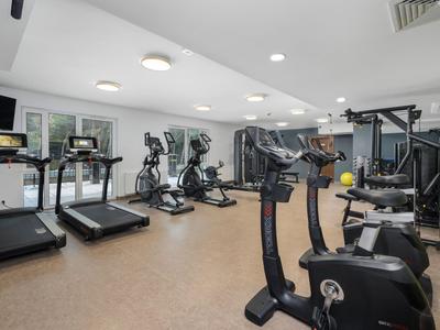 Salle de sport moderne avec tapis de course, vélos et appareils de musculation dans une pièce lumineuse.