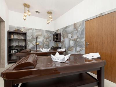 Therapieraum mit Massagebank, braunen Ledermöbeln und dekorativer Wandgestaltung.