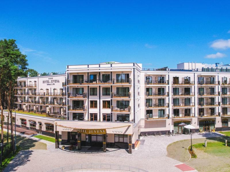 Modernes Hotelgebäude mit mehreren Stockwerken, umgeben von Bäumen unter klarem blauen Himmel