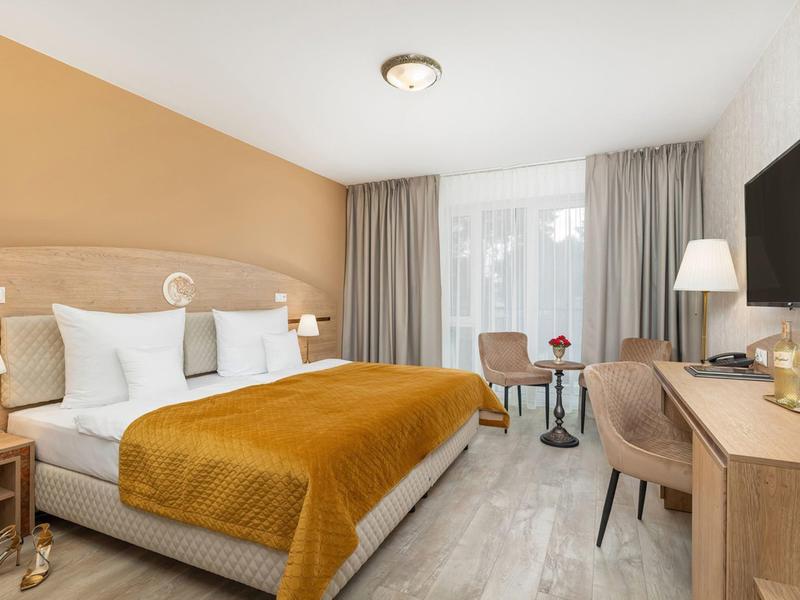 Modernes Hotelzimmer mit großem Bett, gelber Decke und Balkon, hell eingerichtet.