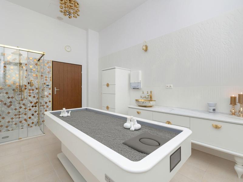 Helles Wellnesszimmer mit Massagetisch, Duschkabine und weißer Kommode mit Dekoration.