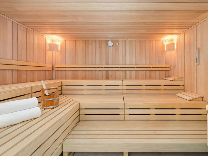 Helle Holzsauna mit mehrstufigen Bänken, Handtüchern und einem Holzeimer.