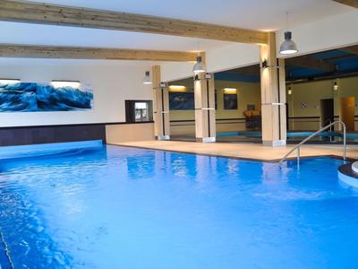 Hallenbad mit blauem Wasser, Holzsäulen und moderner Beleuchtung in einem Hotel.