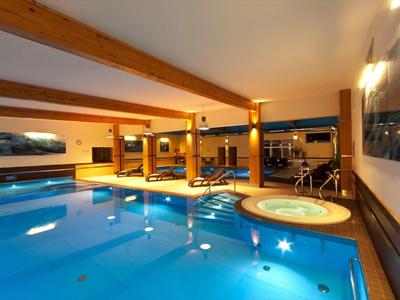 Innenpool mit Whirlpool und Holzdeckenbalken in einem modernen Wellnessbereich.