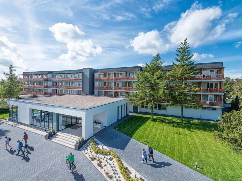 Modernes Hotelgebäude mit großen Fensterflächen, umgeben von Grünflächen und Blaue Himmel.