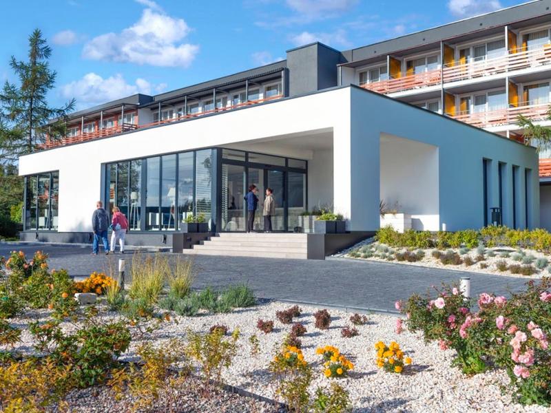 Modernes Hotelgebäude mit großer Glasfassade, weißer Fassade und gepflegtem Vorgarten.