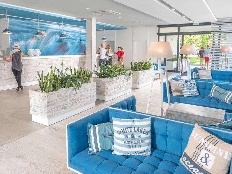 Helle Hotellobby mit blauen Sesseln, Spiegelwand und Rezeption im Hintergrund