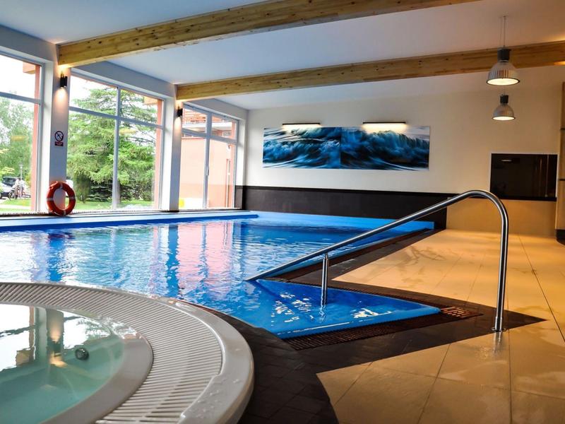 Innenpoolbereich mit Schwimmbecken, Whirlpool und großen Fenstern mit Blick ins Grüne.