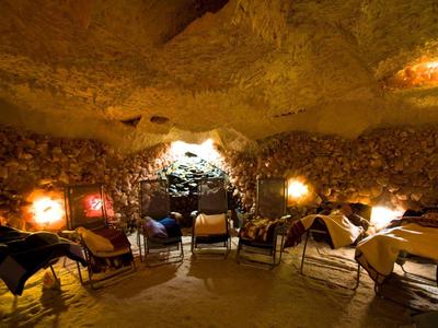 Gemütlicher Innenraum einer Höhlenunterkunft mit Tischen und Stühlen in warmem Licht.