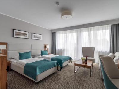 Moderne hotelkamer met twee bedden, fauteuil, salontafel en grote ramen met gordijnen.