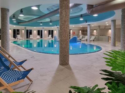 Binnenzwembad met blauw water, ligstoelen en decoratieve zuilen in een hotel.