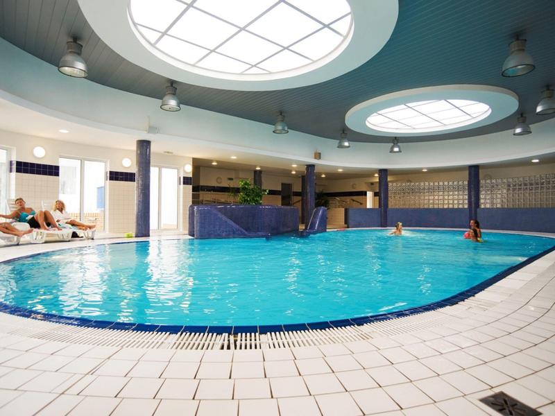 Großer Innenpool mit runden Deckenfenstern und Liegestühlen am Rand.