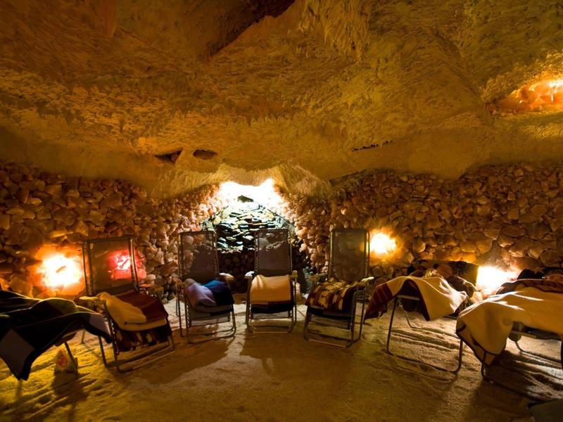 Gemütlicher Innenraum einer Höhlenunterkunft mit Tischen und Stühlen in warmem Licht.