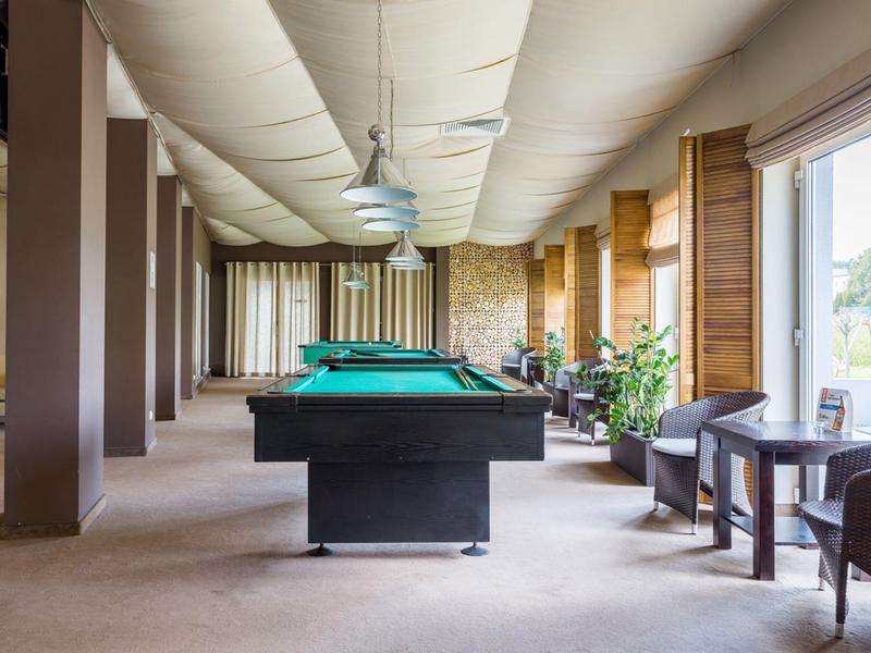 Hell beleuchteter Raum mit Billardtisch, Sitzgelegenheiten und großen Fenstern mit Blick nach draußen.