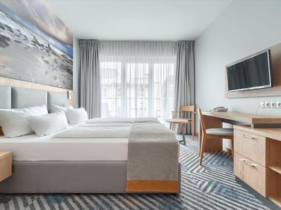 Hell eingerichtetes Hotelzimmer mit zwei Betten, Schreibtisch und Fernseher an der Wand.