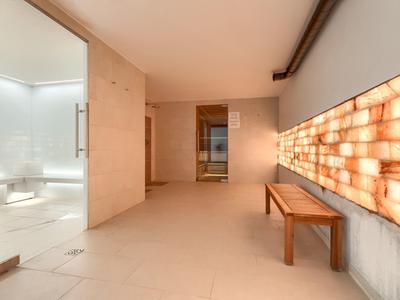 Moderner Wellnessbereich mit Salzsteinwand, Holzbänken und Zugang zu einem Duschbereich.